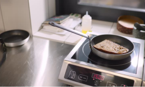 A slice of bread toasts in a pan on a flat induction cooker cooktop, demonstrating its compatibility with standard flat-bottomed cookware.