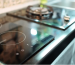 A sleek induction cooker sits beside a gas cooktop in a modern kitchen, highlighting its design and the need for residual heat awareness.